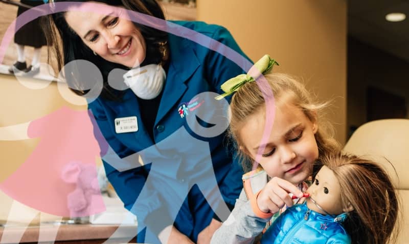 doctor working with a young patient while she brushes her dolls teeth