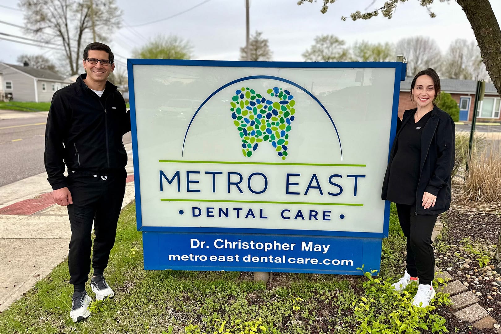 Dr. May and Dr. Lexi standing by Metro East Dental Care exterior sign