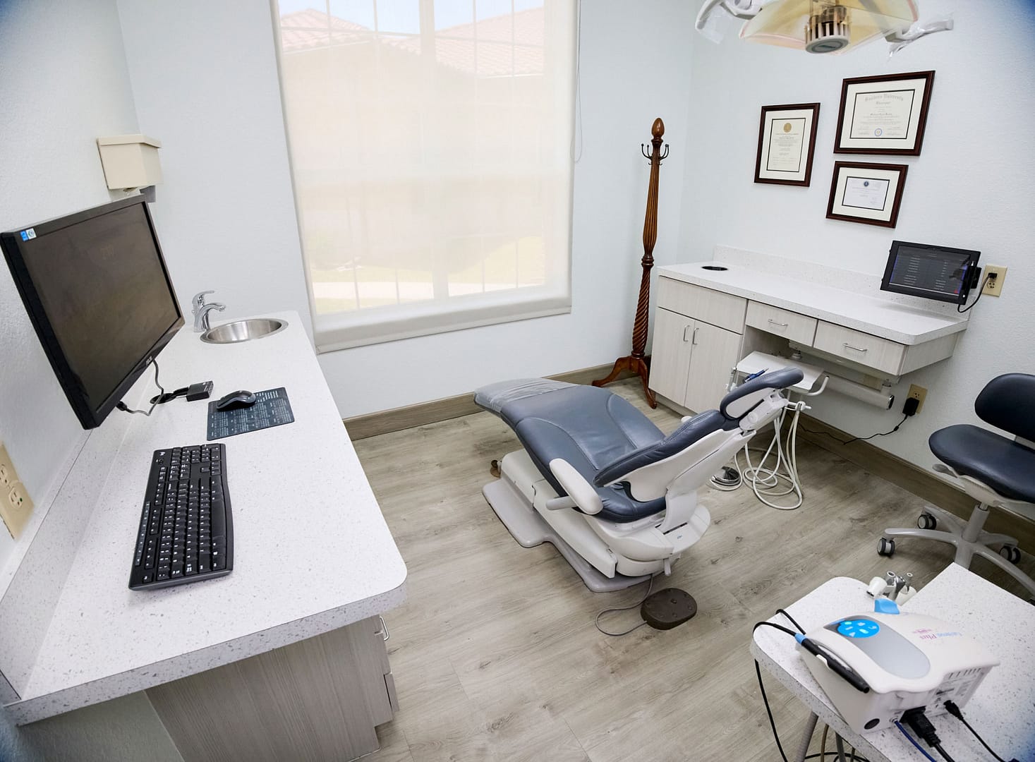 exam room with dental chair and equipment, light brown cabinets with white countertops, and light brown wood floor