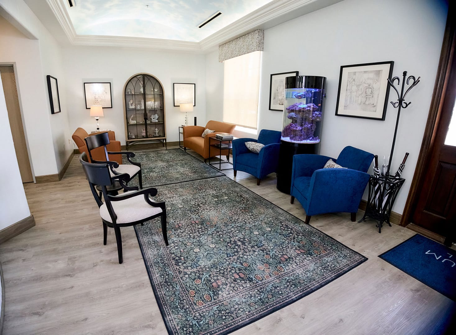 reception area with 2 area rugs on light brown wood floors, coat rack/umbrella stand, fish tank, curio cabinet, lamps on tables and chairs and couches for seating