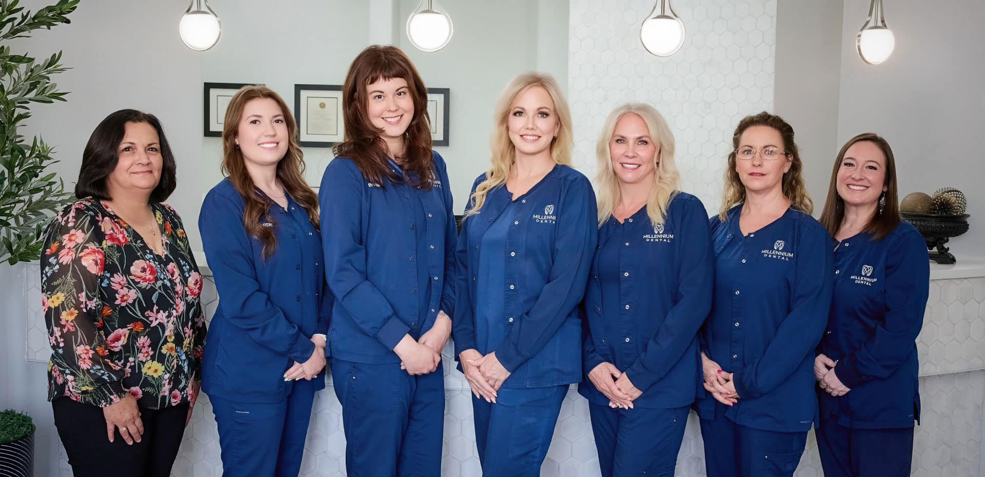 Millennium Dental team wearing blue scrubs posing for a picture in front of the front desk inside the office