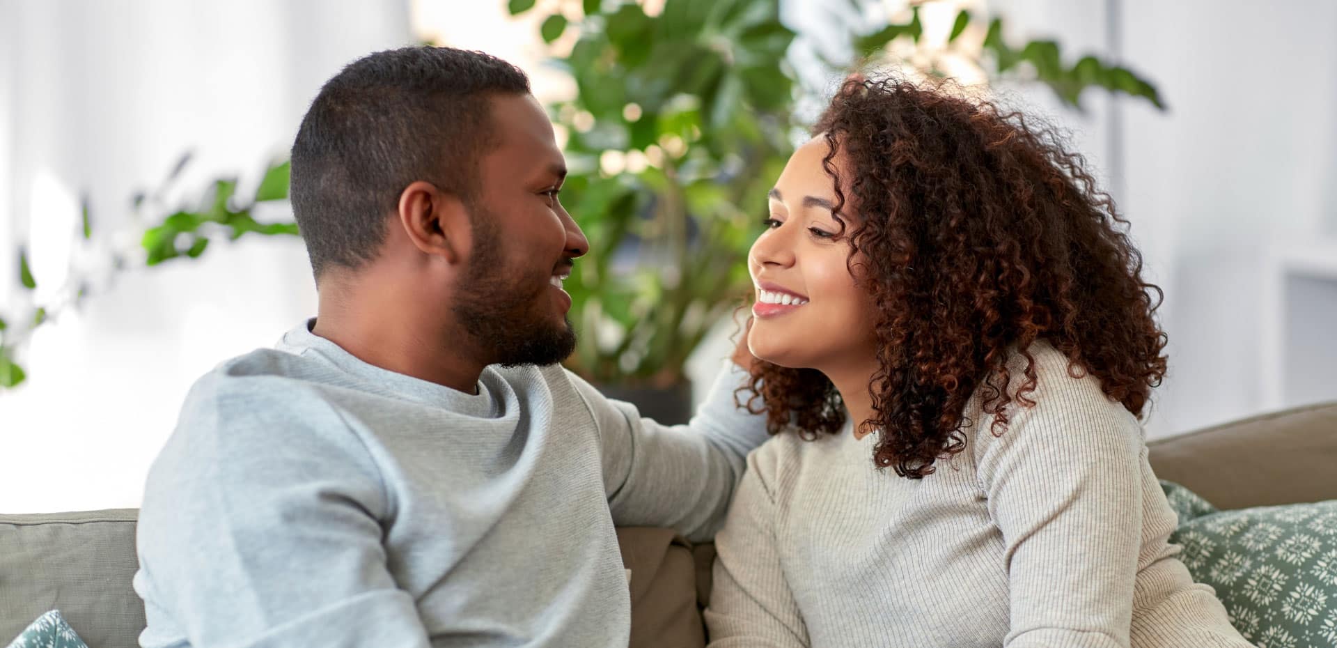 young african american couple smiling at each other while sitting on couch in living room