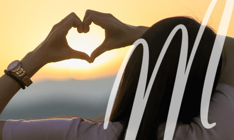 woman making heart shape with her hands over the sunset