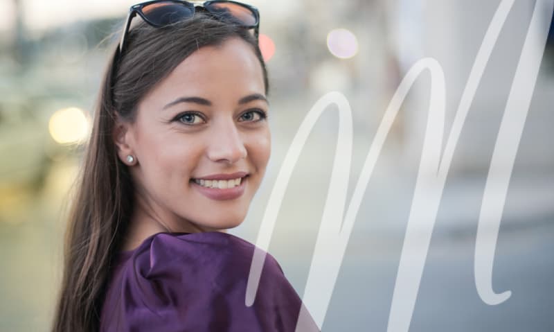 woman smiling with glasses on her head while wearing a purple top