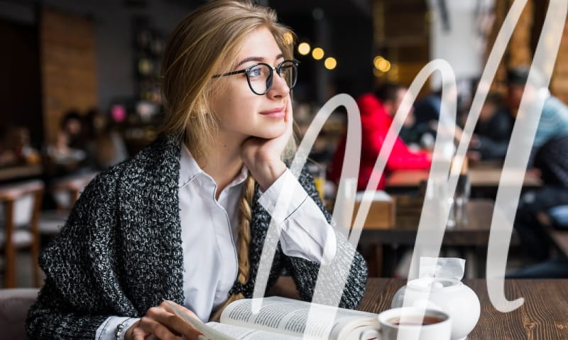 woman in glasses looks up from her book and smiles