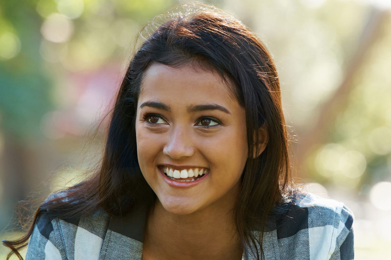 attractive young ethnic woman looking to the left and smiling while outside