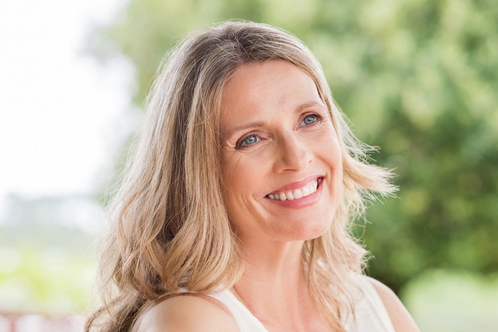 older woman with long blond hair sitting outside looking to the right and smiling