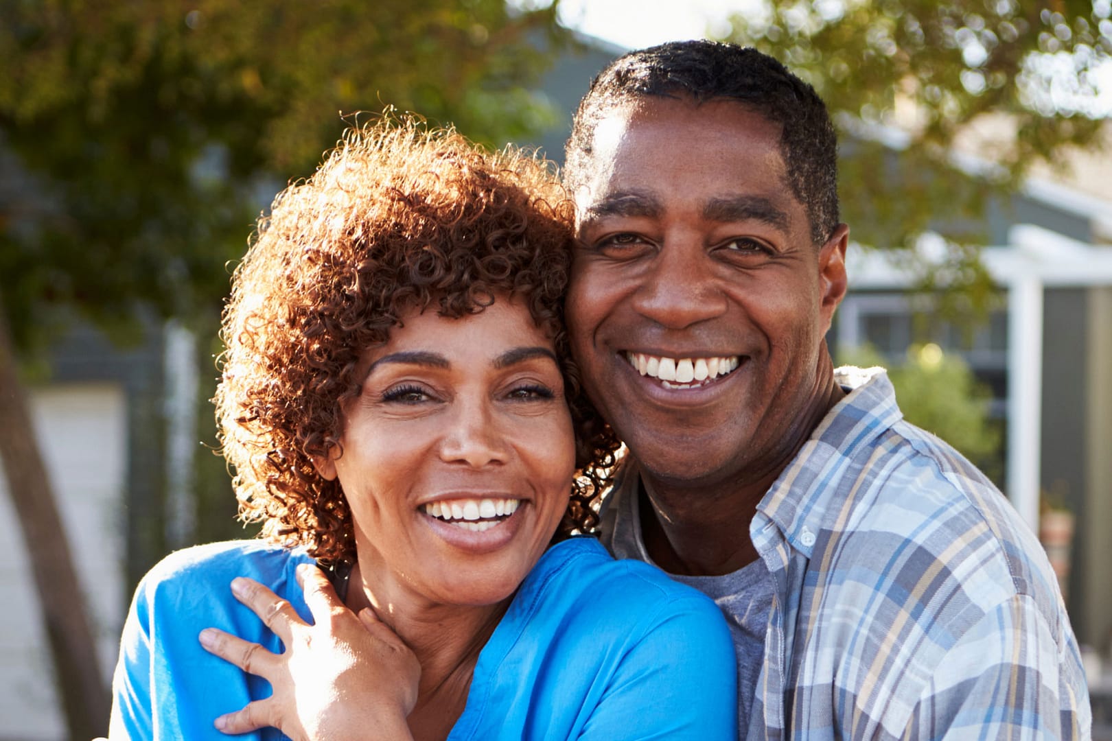 older african american couple posing for the camera standing in front of their house