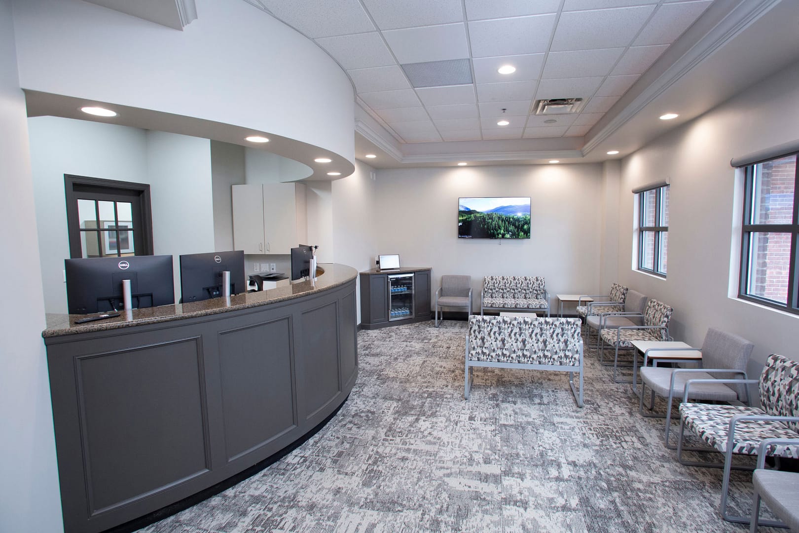 front desk next to reception area with seating, TV on back wall, and refreshment area in the corner