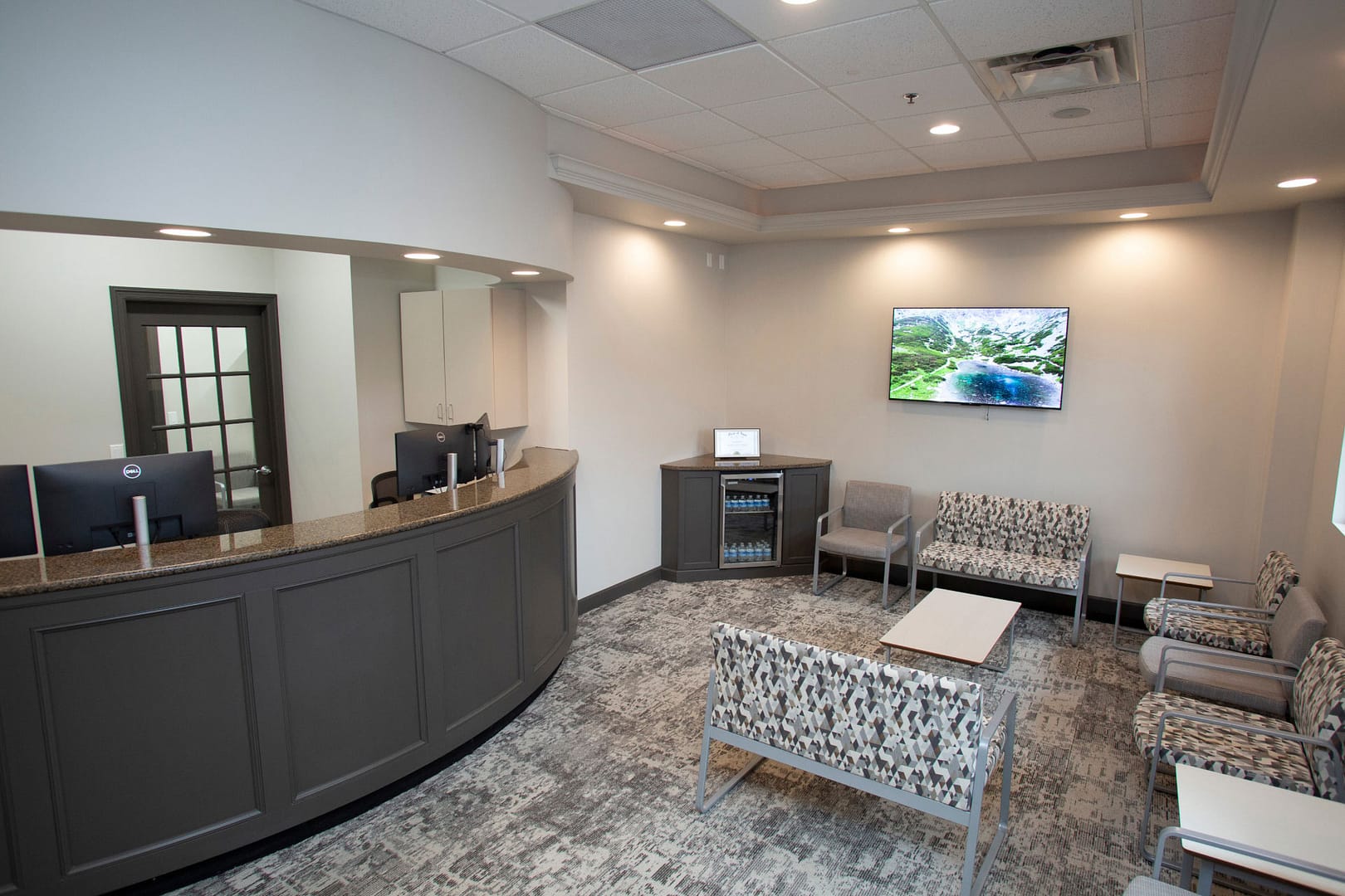 front desk next to reception area with seating, TV on back wall, and refreshment area in the corner