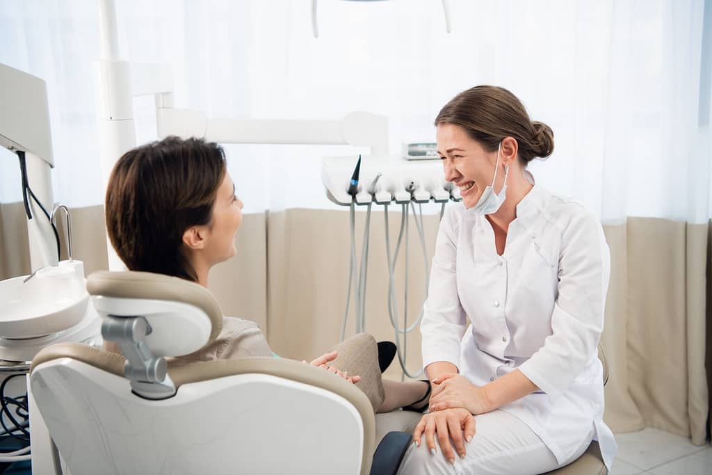 Young female doctor chatting to her patient in her dental office and laughing Root canal and dental crown