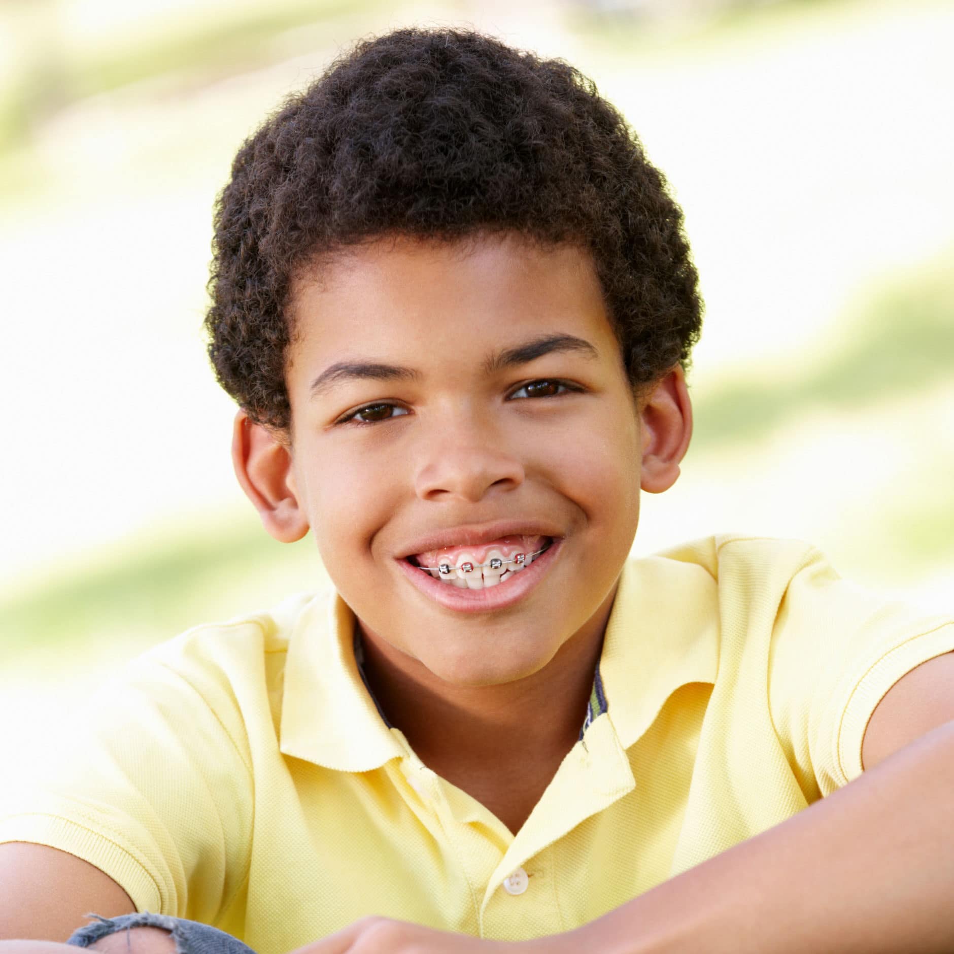 african american boy with braces sitting outside smiling at camera