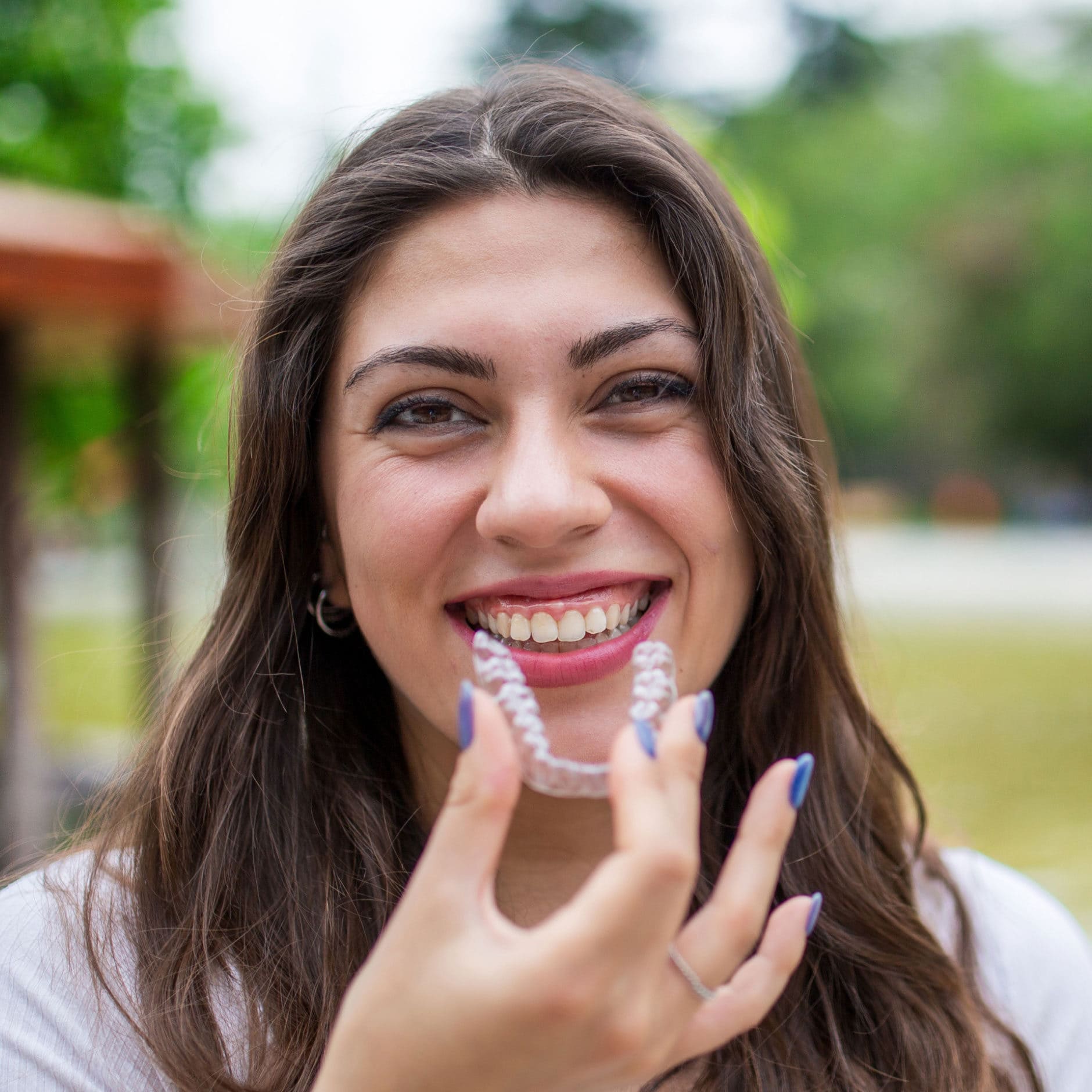 woman holding invisalign aligner in park setting with pond in background
