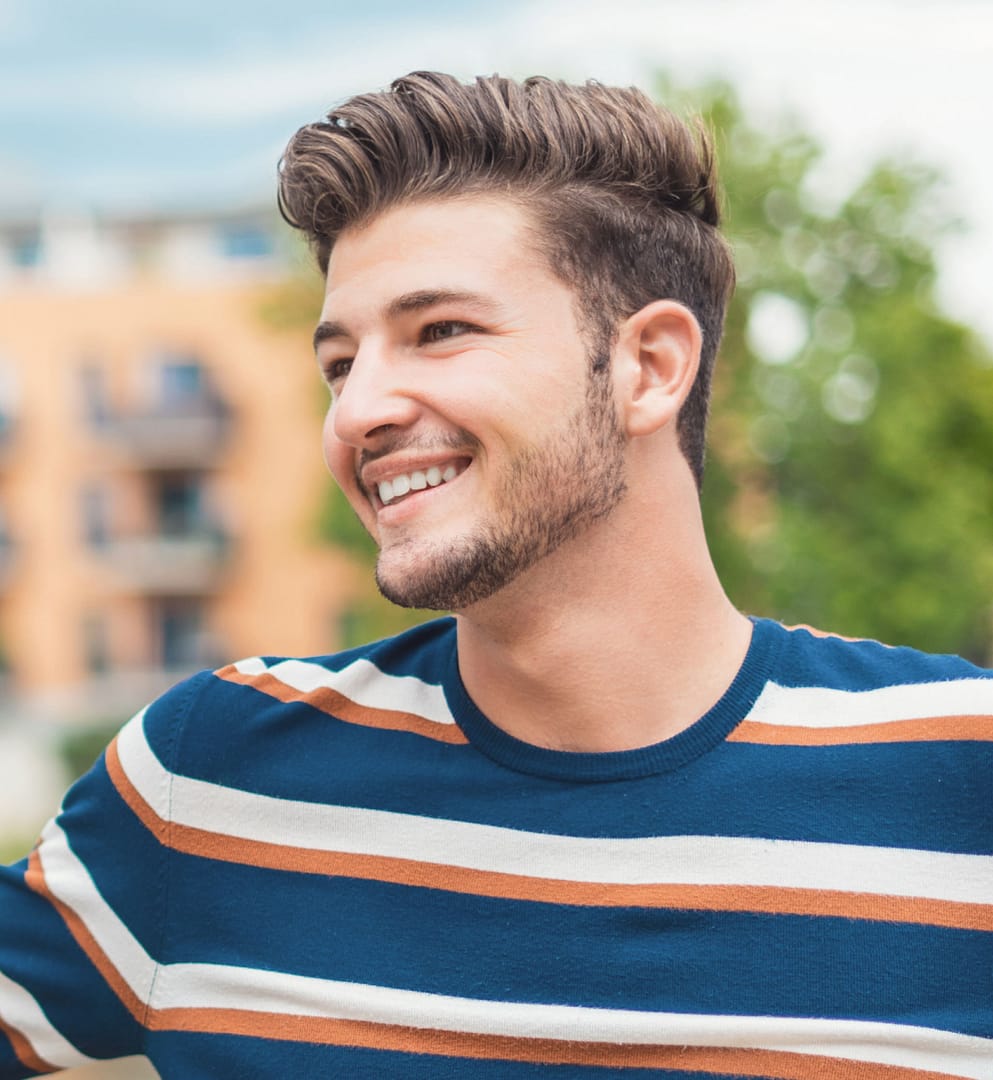 young man wearing striped shirt outside smiling