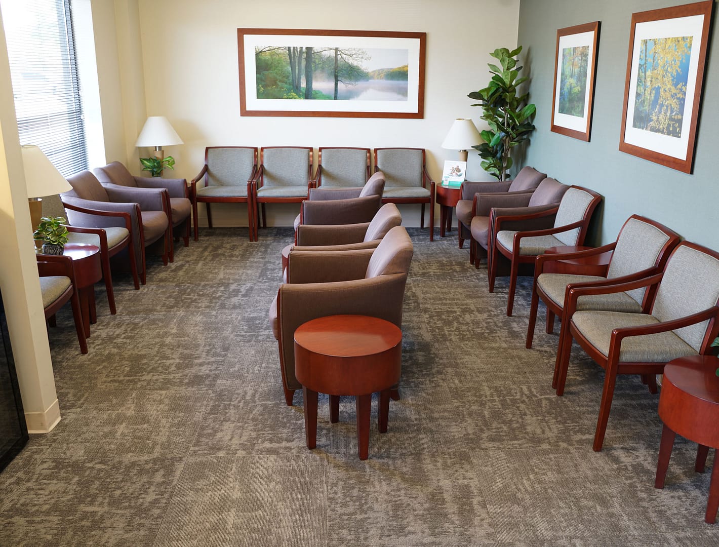 reception area with chairs for seating, nature photos on walls, and tables with lamps, fake tree in corner