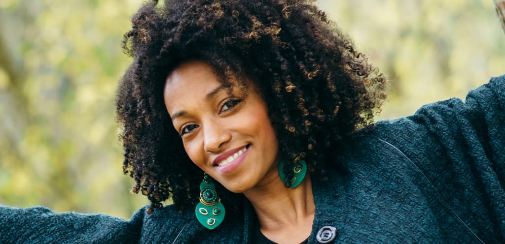young african american woman smiling outside with arms spread wide